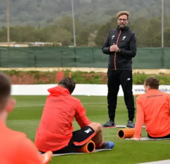 Jürgen Klopp stands to address his football players, who are sat with their backs to camera all wearing the same red jacket, during what he describes as a ‘pre-season training’ camp in La Manga in February 2017