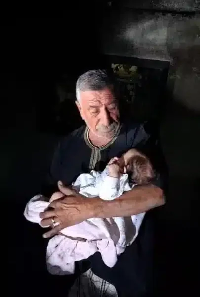 The grandfather of baby Lana Shahada, whose home was attacked by Israeli settlers, holds her and looks down at her