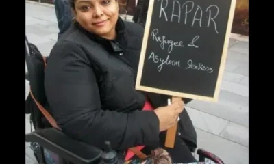 Manjeet Kaur, a human rights campaigner who died, aged 41, in 2020 in Manchester, sought asylum in the UK from Afghanistan in March 2011. In this photo in her wheelchair, she’s smiling holding a chalkboard placard that says 'RAPAR - Refugees and Asylum Seekers'.
