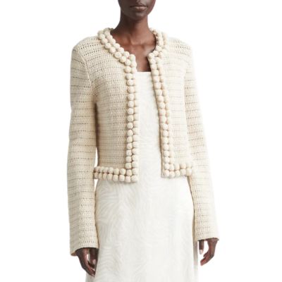 A woman wearing an ivory trimmed cardigan over an over an off-white dress