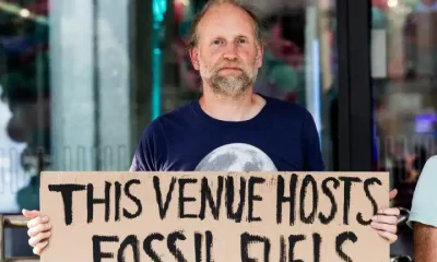 QEII fossil fuel protest Protester holds sign saying This Venue Hosts Fossil Fuels