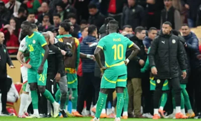 Senegal players standing on the pitch at AFCON final, some wearing only their kits and others with puffer jackets on