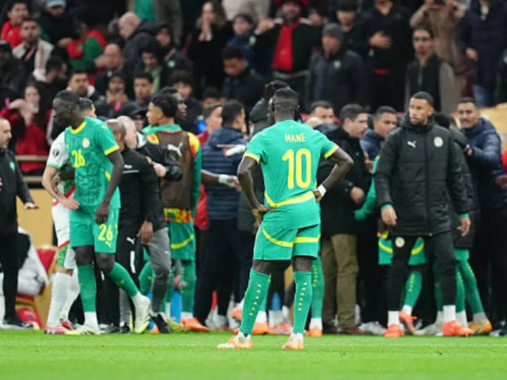 Senegal players standing on the pitch at AFCON final, some wearing only their kits and others with puffer jackets on