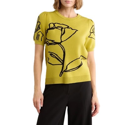 A woman wearing black pants and a yellow-green top with a black floral outline