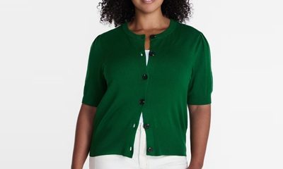 A woman wearing a green short-sleeved cardigan, white top, and white pants