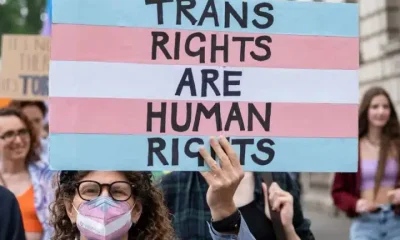 Protester holds a placard in trans pride colours saying Trans Rights Are Human Rights EHRC Code