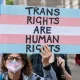 Protester holds a placard in trans pride colours saying Trans Rights Are Human Rights EHRC Code