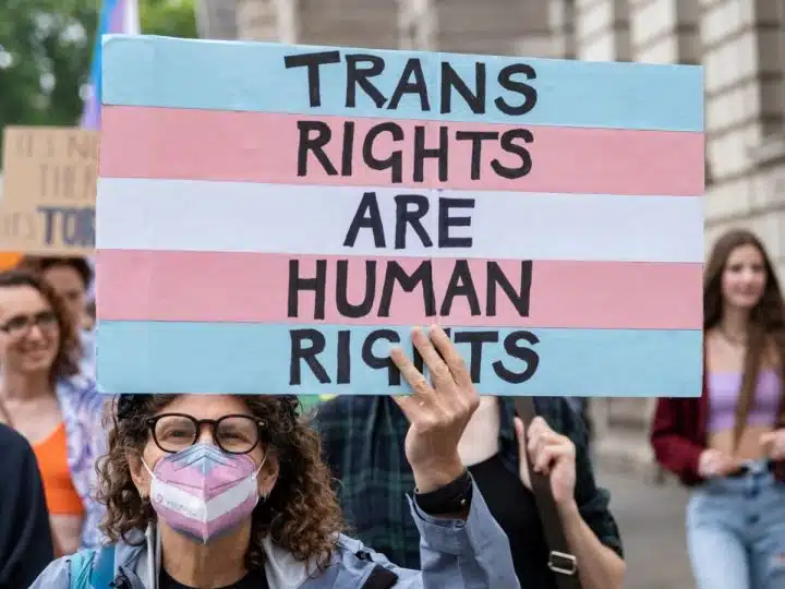 Protester holds a placard in trans pride colours saying Trans Rights Are Human Rights EHRC Code