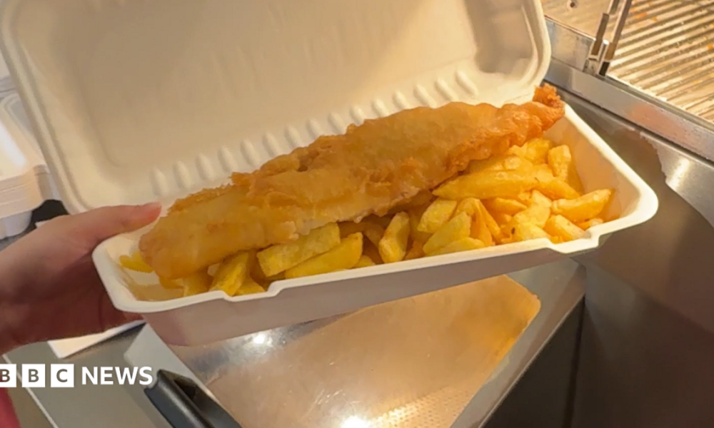 A battered fish and chips in a paper packet.