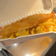 A battered fish and chips in a paper packet.