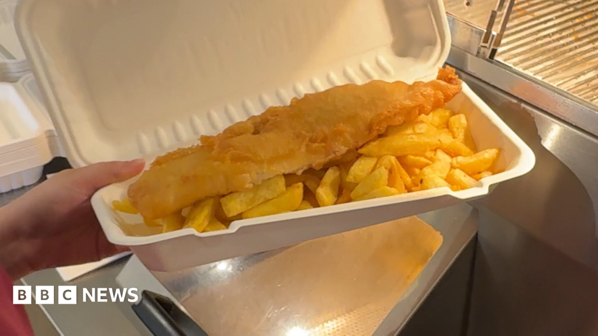 A battered fish and chips in a paper packet.