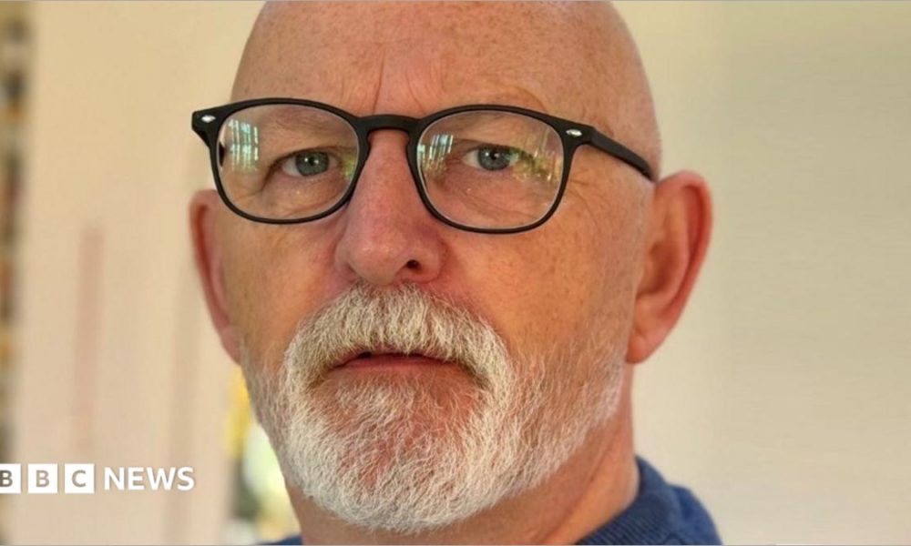 A bald man with a white beard is wearing glasses
