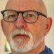 A bald man with a white beard is wearing glasses
