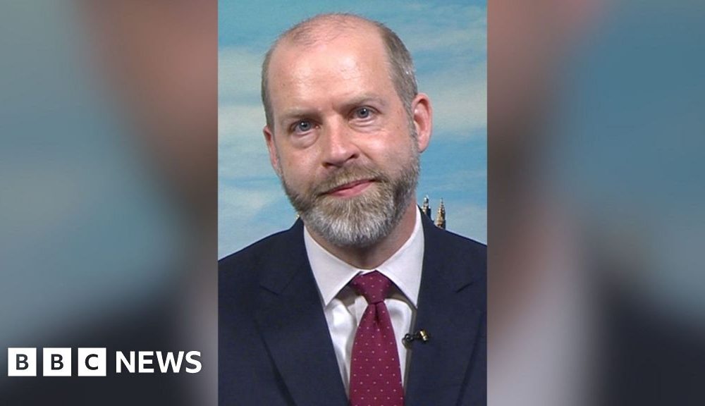 Jonathan Reynolds sat in a studio wearing a suit and a tie