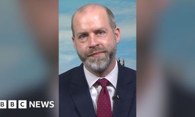 Jonathan Reynolds sat in a studio wearing a suit and a tie