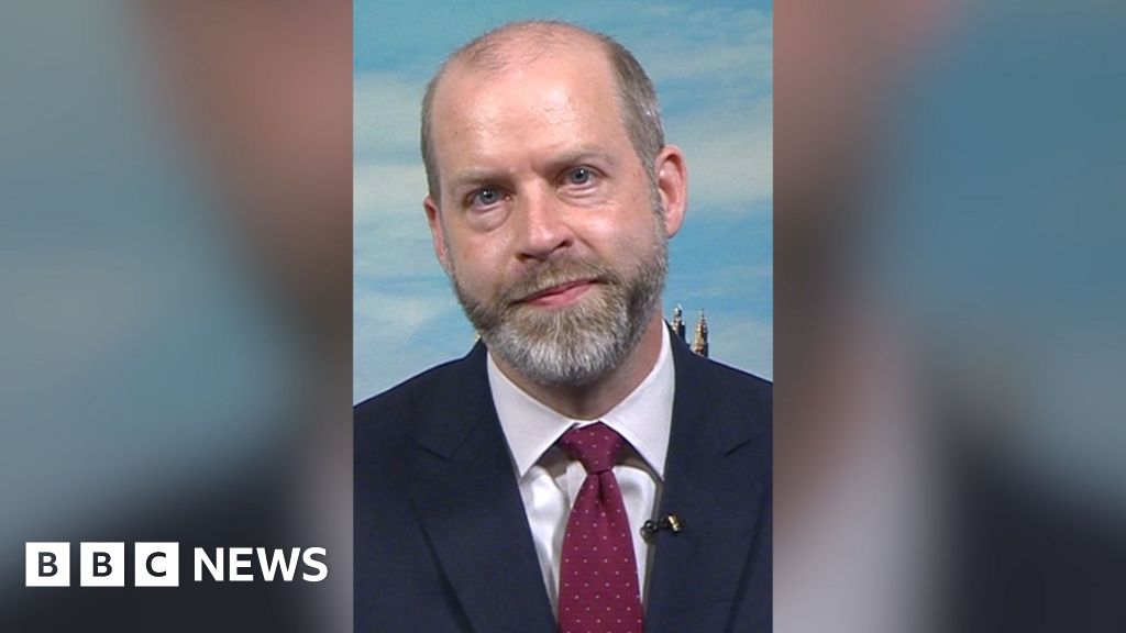 Jonathan Reynolds sat in a studio wearing a suit and a tie