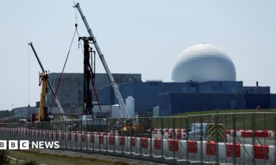 The large white dome of the Sizewell B nuclear power plant is the backdrop of the picture which has construction work and cranes in the foreground. The white dome sits on large square grey coloured buildings.