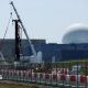 The large white dome of the Sizewell B nuclear power plant is the backdrop of the picture which has construction work and cranes in the foreground. The white dome sits on large square grey coloured buildings.