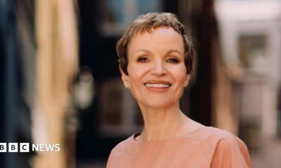 Marcia Kilgore with cropped short brown hair smiling at the camera with a blurred background wearing a nude coloured round neck top