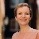 Marcia Kilgore with cropped short brown hair smiling at the camera with a blurred background wearing a nude coloured round neck top