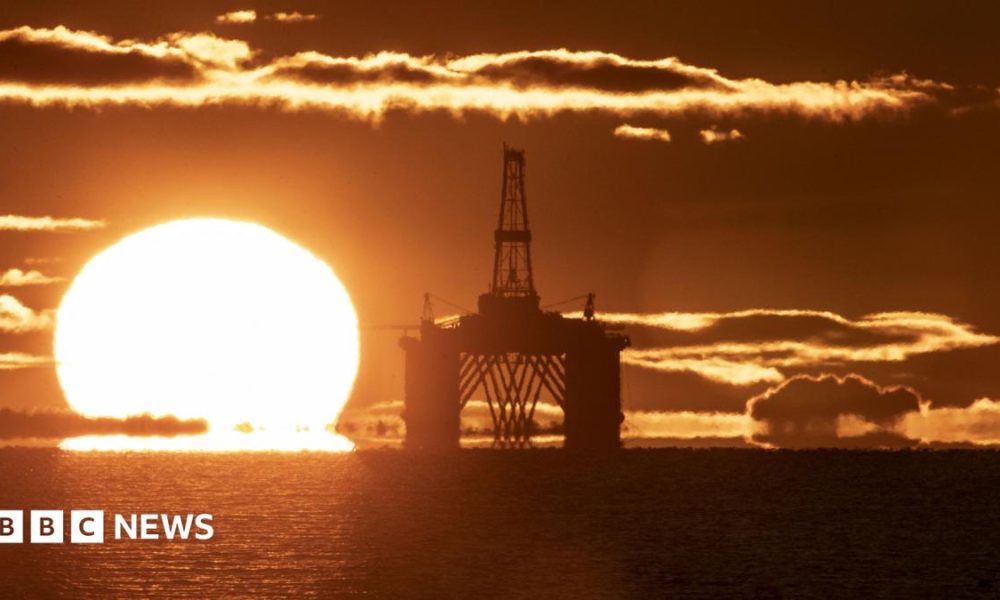 The sun on he horizon behind an oil and gas platform in the North Sea. The sea is calm and the whole scene is a vivid orange colour.