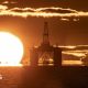 The sun on he horizon behind an oil and gas platform in the North Sea. The sea is calm and the whole scene is a vivid orange colour.