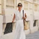 PARIS, FRANCE - MAY 26: Diane Batoukina wears light brown hair with a center part pulled into a low bun, black oversized square sunglasses, a white cotton short-sleeve blouse with a ruffle-trim split neckline and lace inset detailing by Vanessa Bruno, a white high-waisted maxi skirt with a drawstring waist, tiered gathered construction and lace inset panels by Vanessa Bruno, a silver-tone rectangular watch with a dark strap by Chanel, a beige woven shoulder bag with a brown leather shoulder strap by Vanessa Bruno, open toe black leather block heels shoes, during a street style fashion photo session, on May 26, 2026 in Paris, France. (Photo by Edward Berthelot/Getty Images)