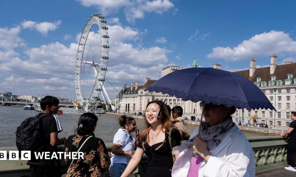 People walk on a bridge over the Thames in London using an umbrella for shade with strong sunshine overhead.