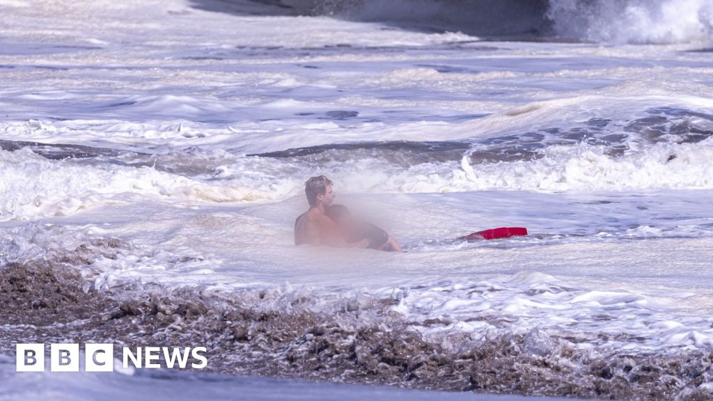 A life guard holds a child in the ocean.