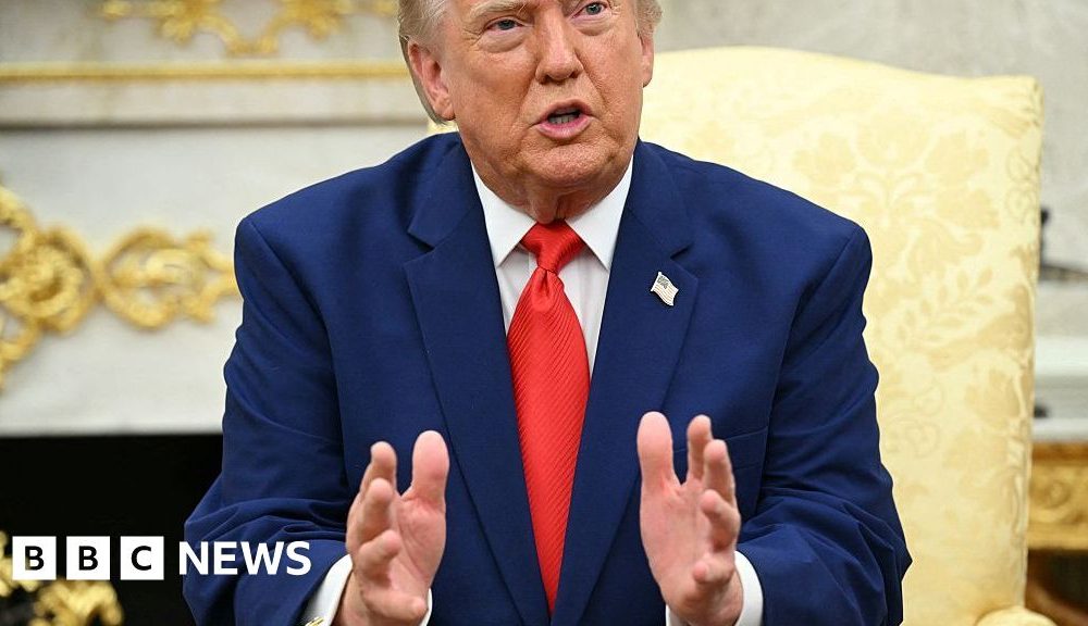 President Donald Trump wearing a blue suit and red tie, talks to reporters.