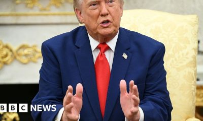 President Donald Trump wearing a blue suit and red tie, talks to reporters.