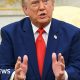 President Donald Trump wearing a blue suit and red tie, talks to reporters.