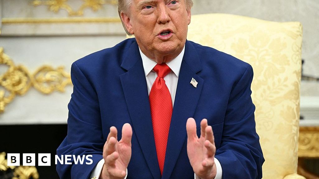 President Donald Trump wearing a blue suit and red tie, talks to reporters.