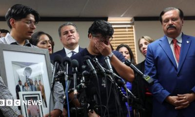 A man holds his hands over his eyes as he stands before a bank of microphones and a man holding up pictures of Lorenzo Salgado Araujo