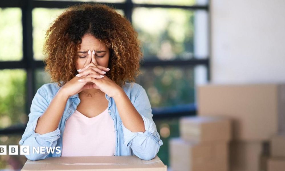 A woman with her head in her hands surrounded by boxes