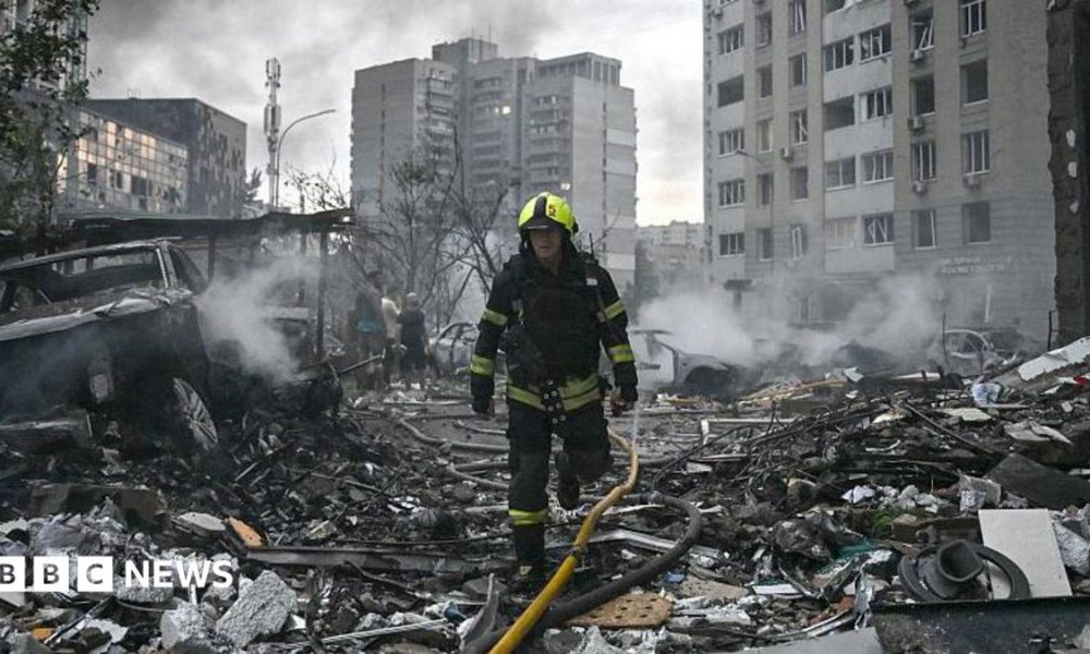Sarah Rainsford in a brown shirt with short sleeves in front of rubble in Kyiv