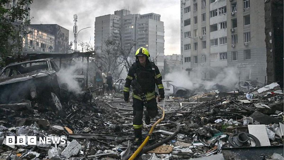 Sarah Rainsford in a brown shirt with short sleeves in front of rubble in Kyiv