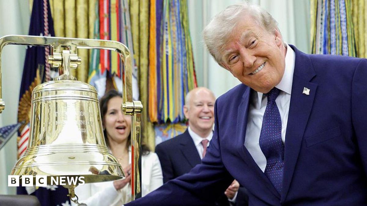 President Donald Trump ringing the opening bell in the Oval Office on Monday. The US president is smiling at the cameras as he rings the big gold bell. He is wearing a dark blue suite, with a dark blue spotted tie and a white shirt.