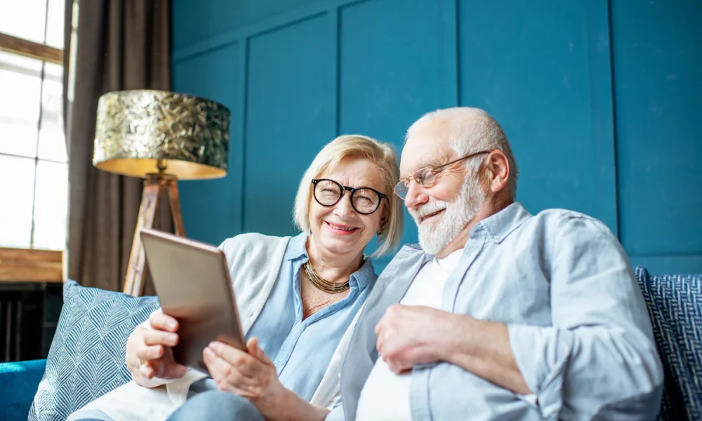 Elderly couple at home, researching the pros and cons of equity release in their living room with blue furniture and walls.