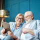 Elderly couple at home, researching the pros and cons of equity release in their living room with blue furniture and walls.