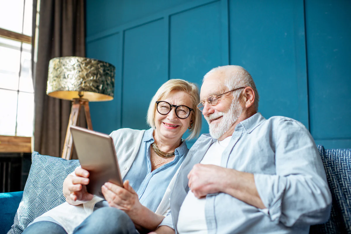 Elderly couple at home, researching the pros and cons of equity release in their living room with blue furniture and walls.