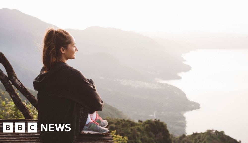 A young woman sits on an elevated platform overlooking the coastline.