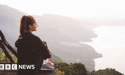 A young woman sits on an elevated platform overlooking the coastline.