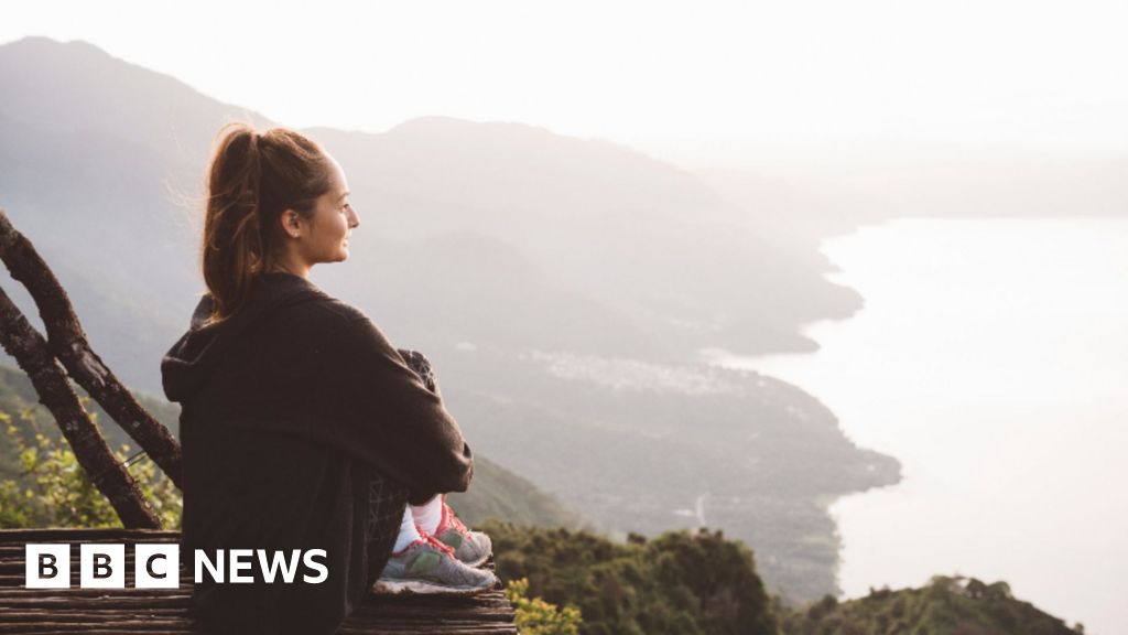 A young woman sits on an elevated platform overlooking the coastline.