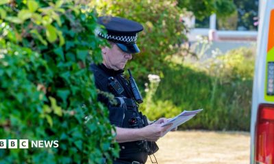 A police officer looks down at a sheet of paper while wearing uniform next to a bush and police van outside Widdecombe's home on Friday.