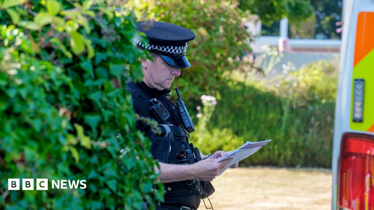 A police officer looks down at a sheet of paper while wearing uniform next to a bush and police van outside Widdecombe's home on Friday.
