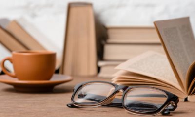 beige books stacked on a table, with eyeglasses and a coffee cup also