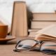 beige books stacked on a table, with eyeglasses and a coffee cup also