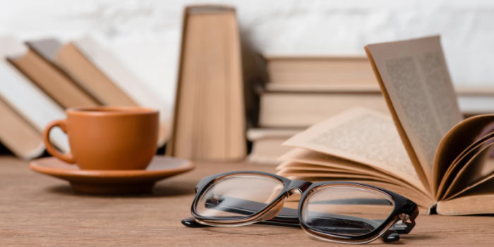 beige books stacked on a table, with eyeglasses and a coffee cup also