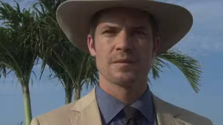 Timothy Olyphant wearing a hat with palm trees behind in the Justified pilot Fire in the Hole.